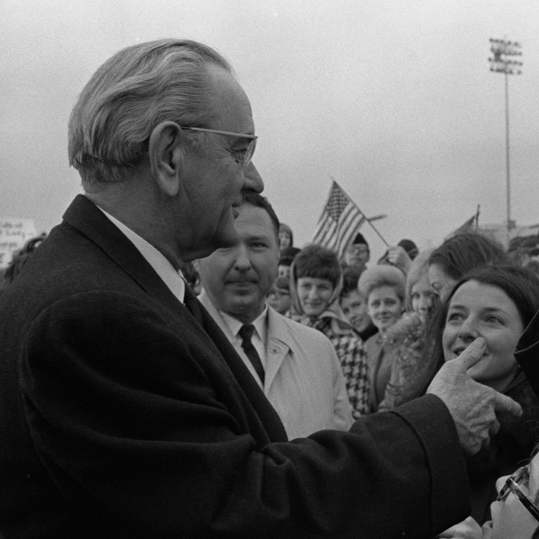 An officer salutes President Johnson as he shakes hands with supporters.